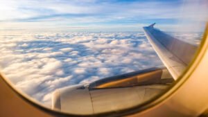 View from an airplane window seat over white clouds and blue sky during a long-haul flight