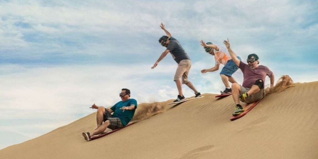 People sandboarding down a dune in Huacachina, Peru