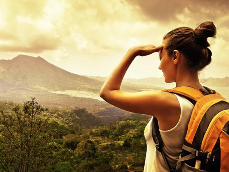 Solo female traveler with a backpack looking out over a vast African landscape at golden hour