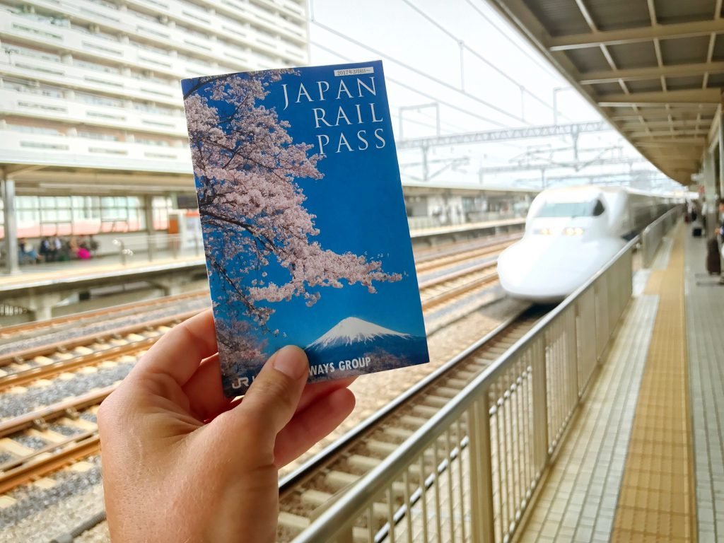 Japan Rail Pass booklet held up at a Shinkansen station platform - Japan travel guide